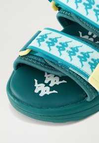 Sandalo teal con cinturini regolabili, decorato con motivi ripetuti di logo bianco e teal e loghi bianchi stampati sulla soletta.