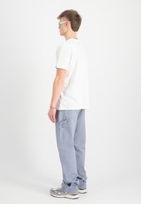 Camiseta blanca de manga corta, pantalones cargo gris claro con bolsillos y zapatillas deportivas grises. La persona lleva gafas de sol con un tinte azul.