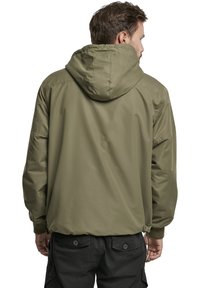 Veste à capuche olive avec une texture lisse, des poignets élastiques et un cordon de serrage à la taille. La vue arrière montre des détails de couture.