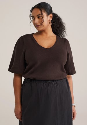 Brun strikket top med korte pufærmer og V-hals, båret med en sort nederdel med elastisk talje. Enkel og tekstureret design.