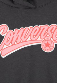 Σκούρο γκρι φούτερ με μια έντονη ροζ επιγραφή "Converse" και κυκλικό γραφικό "Chuck Taylor All Star" με σχέδιο αστεριού.