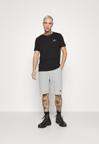 Svart bomull T-skjorte og grå shorts, med logo, rett snitt og ribbet halslinning. Modell som har på seg svarte kampsko.