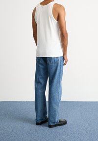 Top de tirantes blanco acanalado y jeans holgados de color azul claro, visto desde atrás. Zapatos negros con un patrón texturizado completan el atuendo.