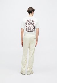 T-shirt branca com um design gráfico bordô nas costas apresentando uma borboleta e texto. Combinada com calças largas de cor creme.