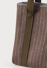 Καφέ μαλλί τσάντα ώμου με κάθετους ανοιχτούς ρίγες και σκούρα καφέ πλεκτή λαβή σε λευκό φόντο.