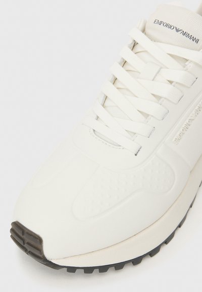 Valged tennisjalad, millel on sile nahkpealne, tekstuursete aktsentidega ja ühtlaste lukkudega. Varustatud tugeva musta kummitaldaga. Brändi logo keelega.