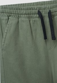 Spodnie dresowe w oliwkowej zieleni o fakturowanej powierzchni, z elastycznym pasem i czarnymi troczkami. Posiadają boczne kieszenie oraz wzmocnione szwy.