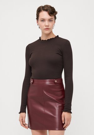 Brown long-sleeve top with ruffled neckline paired with a maroon faux leather mini skirt featuring snap buttons and smooth texture.