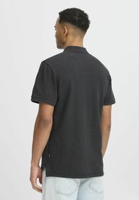 Svart kortermet polo-shirt laget av teksturert stoff, med en klassisk krage og sideslisser i kanten for bedre bevegelsesfrihet.