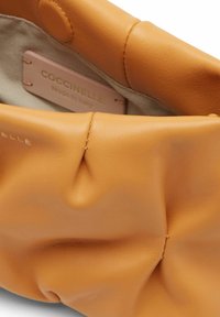 Sac en cuir orange avec une texture douce et froissée et un détail de couture visible. Dispose d'une doublure en tissu de couleur claire et d'une étiquette de marque à l'intérieur.
