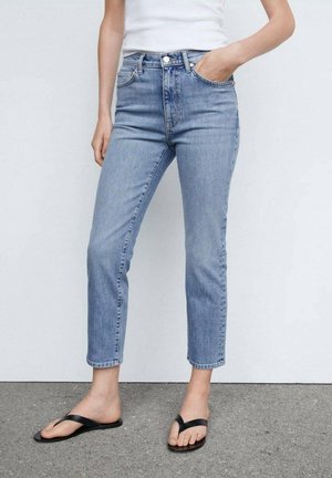 Jeans de tiro alto azules claros con corte recto y largo hasta los tobillos, que cuentan con bolsillos estándar y cierre de botón, combinados con chanclas negras.