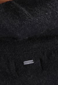 Tessuto nero a maglia con una morbida texture, caratterizzato da una piccola etichetta argentata cucita nella parte inferiore, che indica il nome del marchio.