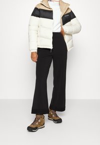 En puffjacka i kräm, beige och svart med hög krage, kombinerad med svarta byxor och bruna vandringsstövlar med färgglada snören.