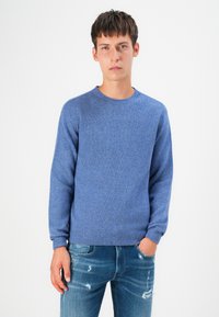 Blauwe gebreide trui met een ronde hals en geribde manchetten; gecombineerd met vervaagde spijkerbroek met een ontspannen pasvorm en lichte slijtage.
