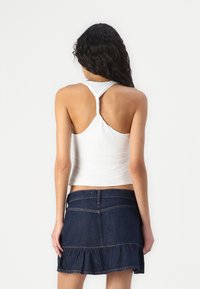 Biały dopasowany top na ramiączkach z plecami w stylu racerback, w połączeniu z ciemnogranatową spódnicą dżinsową z falbaną u dołu i widocznymi detalami przeszycia.