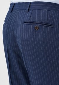 Marineblau gestreifte Hose aus strukturiertem Stoff, mit zwei Gesäßtaschen mit braunen Knöpfen und einer taillierten Passform.