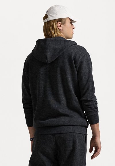 Hoodie cinza escuro com uma textura suave, apresentando um capuz grande, punhos canelados e um corte descontraído. Usado com um boné branco.