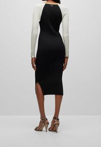 Robe midi côtelée noir et blanc à manches longues, avec une fente latérale et des détails de boutons sur les poignets. Sublimée par des talons fins à lanières.