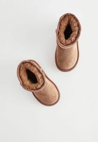 Bruna mockaskinnankelboots med en mjuk pälsfoder, rund tå och sydda detaljer vid skaftet. Designen är enkel och mysig, lämplig för avslappnad användning.
