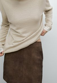 Beżowy dzianinowy sweter z długimi rękawami w połączeniu z brązową zamszową spódnicą. Tkanina jest miękka i teksturowana, cechuje się subtelnym układem i warstwowością.