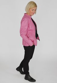 Rosa Lederjacke mit Stehkragen, gerafftem Taillendesign und Reißverschluss. Getragen mit schwarzen Hosen und Knöchelstiefeln.