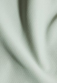 Ljusgrön texturerad tyg med en subtil geometrisk mönstring, slät yta med lätt lyster, draperad för att framhäva veck och konturer.