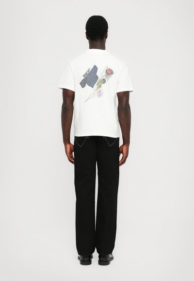 T-shirt bianco a maniche corte con grafica sulla schiena che presenta denim, una rosa e del testo. Abbinato a pantaloni neri e scarpe nere.
