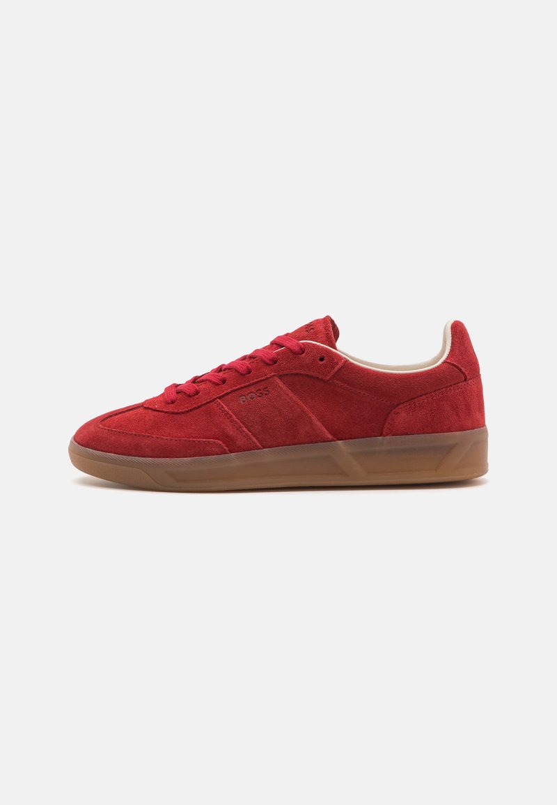 Red suede sneaker with a low profile, lace-up design, and rubber sole. Features a logo detail on the side and tan accents on the collar.