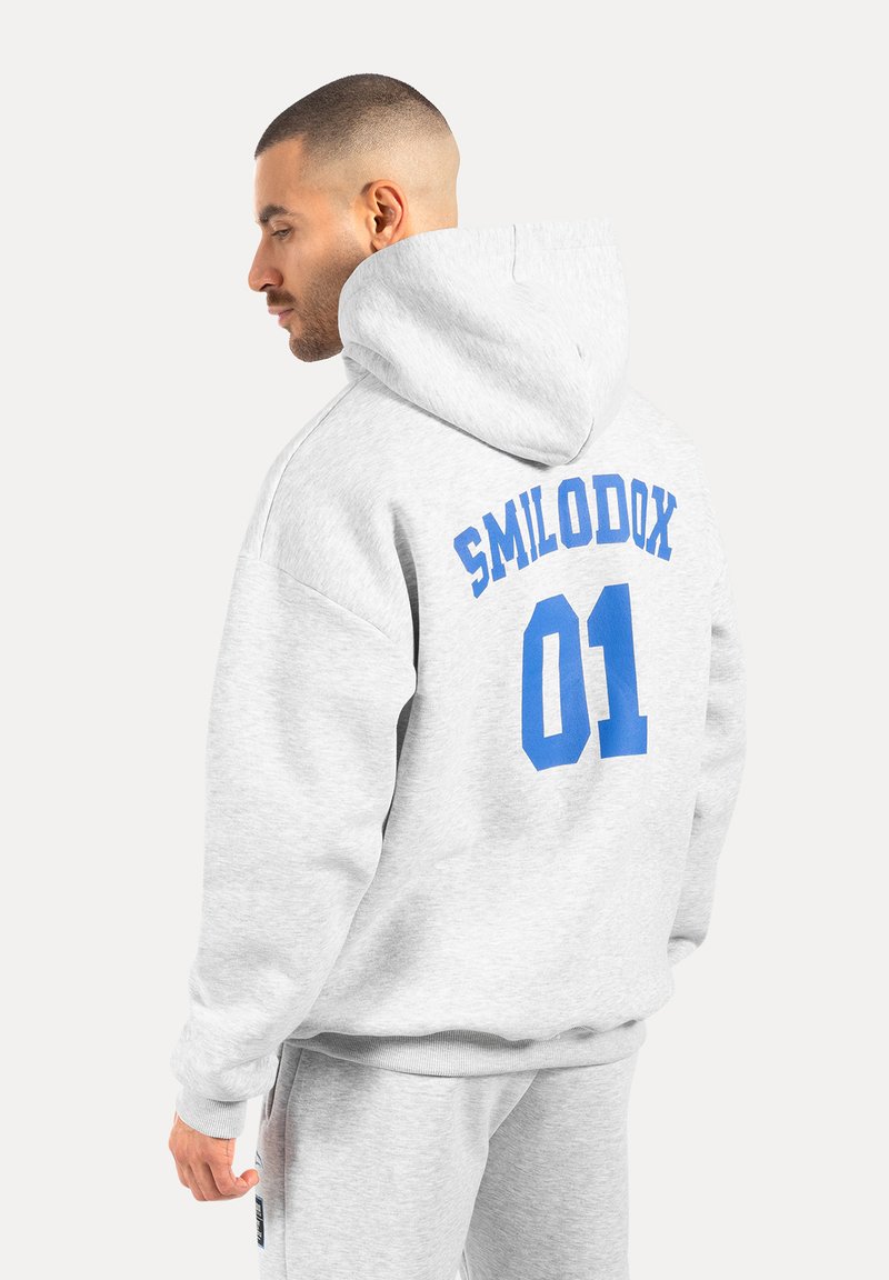 Szara hoodie z kapturem z niebieskim napisem "SMILODOX 01" na plecach. Charakteryzuje się luźnym krojem i ściągaczami na rękawach, wykonana z miękkiego materiału.