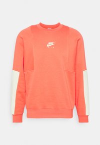 Sweatshirt corail avec un col rond, des manches longues et des accents de panneaux blancs. Présente un logo central Nike Air en blanc sur le devant.