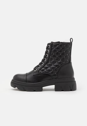 Botte de combat en cuir noir avec une zone de cheville matelassée et cloutée, fermeture à lacets à l'avant, semelle épaisse à crampons et languette à l'arrière.