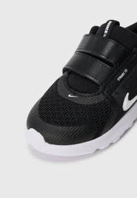 Schwarzer Sportschuh mit einem strukturierten Mesh-Obermaterial und glattem, synthetischen Overlay. Verfügt über einen Klettverschluss und ein weißes Nike-Logo an der Seite.