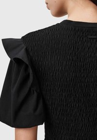 Zwarte shirt met een gerimpelde textuur op de achterkant, met korte, gerimpelde mouwen. Glad stof met een matte afwerking en subtiele stiksels.