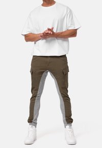 White short-sleeve t-shirt paired with olive green and gray tapered cargo pants featuring side pockets and elastic cuffs. White sneakers.