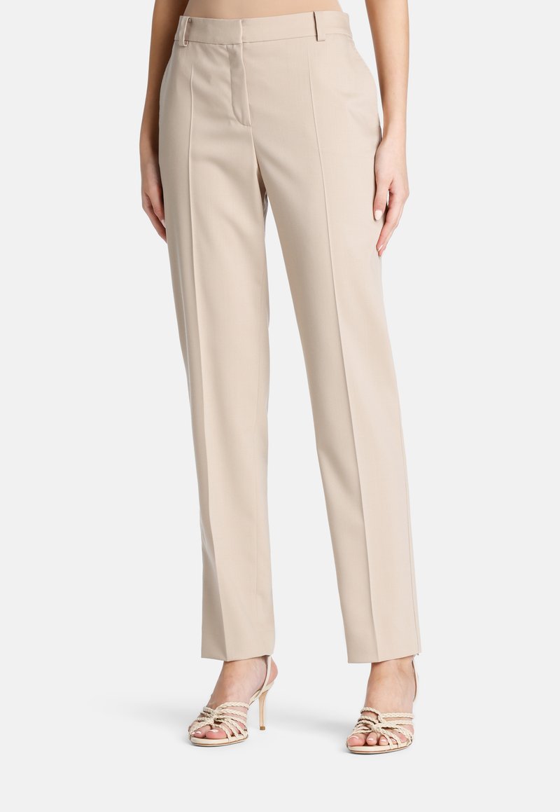 Pantalons beige ajustés avec une coupe droite, des plis à l'avant et une texture lisse, associés à des talons avec des lanières.