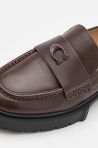 Brown leather loafer with a wide band featuring a raised logo. Textured finish, contrasting stitching, and a rubber sole.