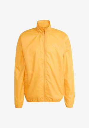 Chaqueta amarilla ligera con cuello alto, cierre completo con cremallera y puños elásticos. Presenta un logo sutil en el pecho y una textura suave.