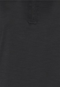 Polo noir avec un tissu texturé et une fermeture éclair à mi-hauteur. Des variations subtiles de couleur ajoutent de la profondeur à l'ensemble du design.