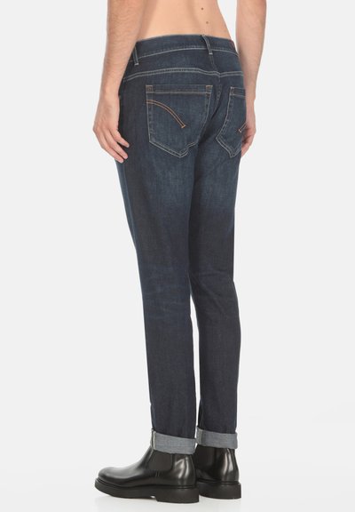 Jeans in denim blu scuro con vestibilità slim, dotati di cinque tasche, leggeri dettagli di cucitura e orli risvoltati sopra stivaletti neri alla caviglia.