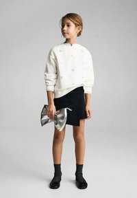 Vit sweatshirt med blommig broderi, svart denimkjol, silverfärgad kläms väska, svarta texturerade strumpor och svarta skor. Enkel design och neutrala nyanser.