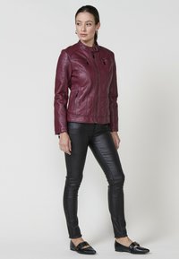 Veste en simili cuir couleur vin avec fermeture éclair sur le devant, col à pression et deux poches zippées ; assortie à un legging noir texturé et des ballerines noires.