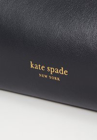 Navy leather handbag with a textured surface and a gold embossed logo reading "kate spade NEW YORK" in a modern font.