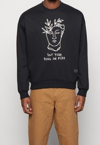 Sudadera de color azul marino oscuro de algodón, con un dibujo lineal minimalista en blanco de un rostro con hojas y el texto "ENCIENDE TU ALMA".