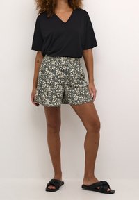 Czarny t-shirt z dekoltem w serek, szorty w kwiatowy wzór w ciemnym granacie i kremie oraz czarne sandały. Szorty mają elastyczną talię i kieszenie.