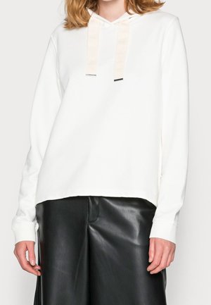 White hooded sweatshirt with long sleeves, featuring a textured fabric and contrasting cream drawstrings. Paired with black leather pants.