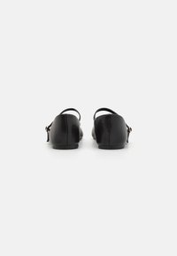 Schwarze Lederschuhe mit glatter Oberfläche, niedrigem Absatz und Knöchelriemen, der mit einem kleinen goldenen Akzent auf der Rückseite versehen ist. Rundlich geformte Zehenpartie.