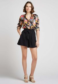 Blouse florale noire, ornée de fleurs roses, bleues et jaunes ; associée à un short noir taille haute avec un détail de lien à l'avant.