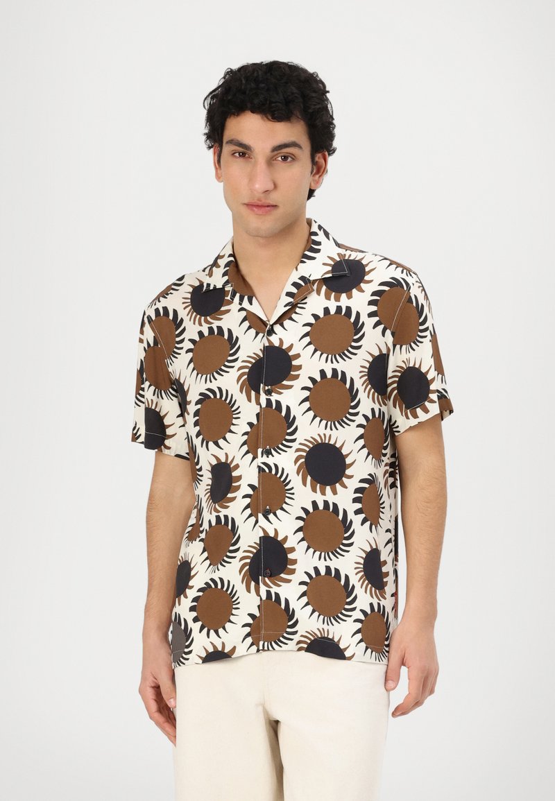 Camicia a maniche corte color crema con motivo a raggi di sole marrone e nero. Presenta una vestibilità comoda e un colletto classico con chiusura a bottoni.