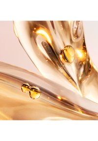 Des gouttes de liquide doré et clair sur une surface lisse et semi-transparente avec des motifs tourbillonnants ; la texture brillante reflète la lumière sur un fond doux.
