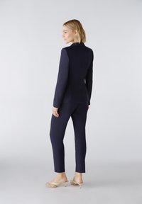 Marineblazer und taillierte Hose, maßgeschneiderte Gestaltung, glatte Textur, minimalistische Nähte, kombiniert mit hellen, hochhackigen Sandalen.